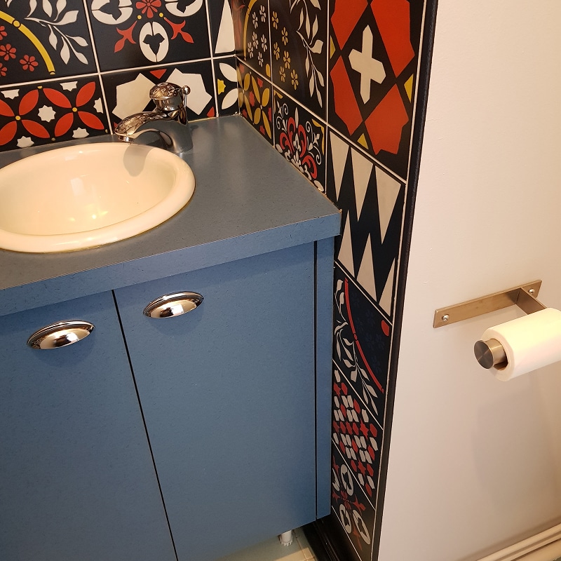 Meuble vasque bleu avec carrelage mural décoratif aux motifs géométriques et porte-papier toilette.