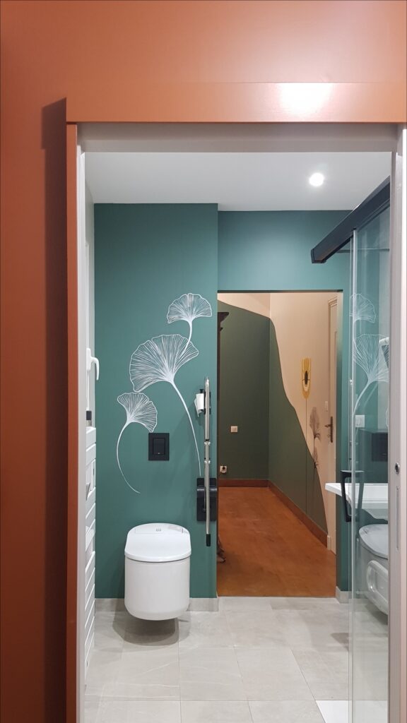 Toilette suspendue blanche devant mur vert canard avec motif ginkgo. Déco de salle de bain moderne et colorée.