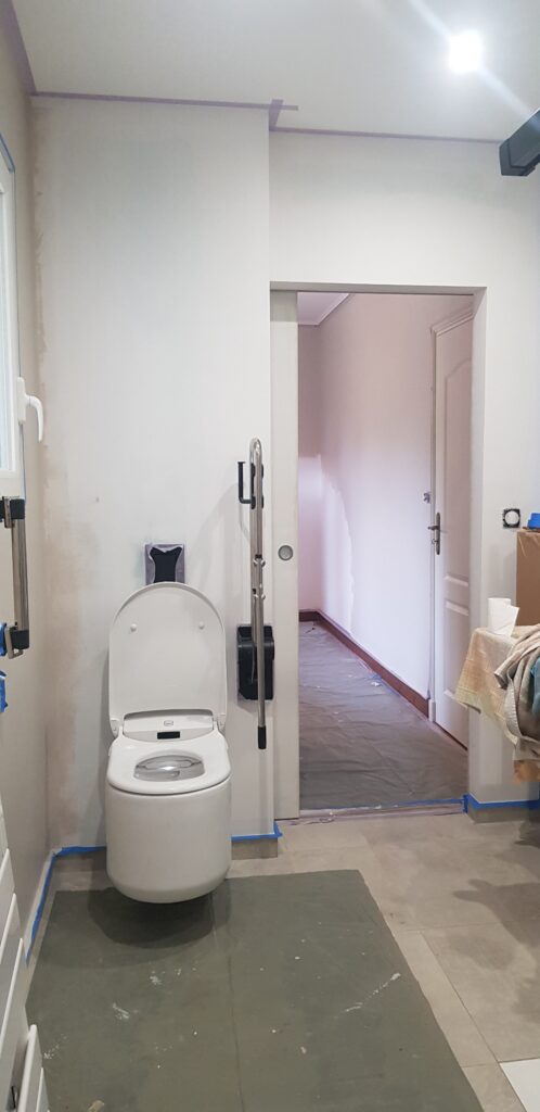 Toilette suspendue blanche PMR avec barre d'appui pour handicapé dans une salle de bain en rénovation.